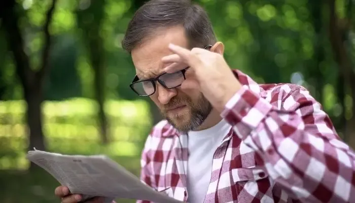 Homme hypermétrope lisant son journal avec des lunettes de vue pour corriger sa vision