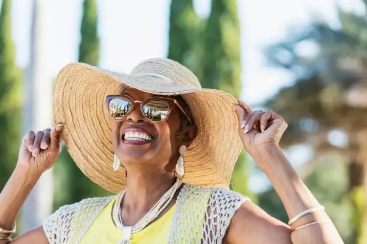 Femme souriante portant des lunettes de soleil et un grand chapeau pendant ses vacances au soleil