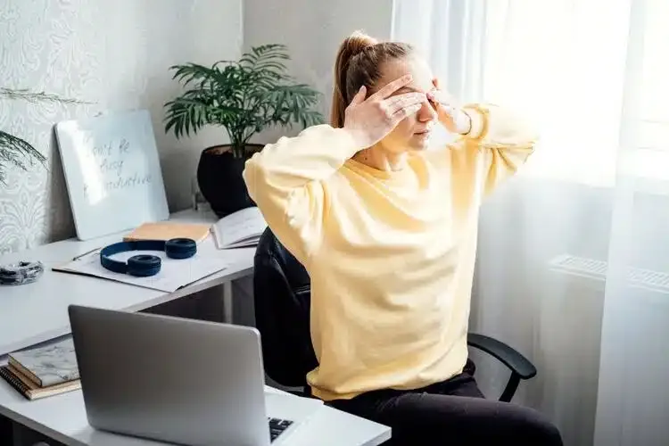 Femme se massant les yeux au travail pour soulager la fatigue oculaire devant l’écran